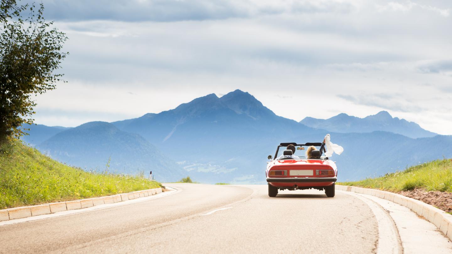 couple in red convertible driving toward mountains