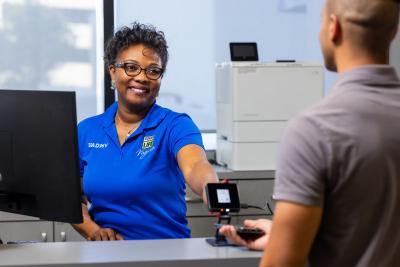 woman in blue shirt behind counter holding device to male customer's phone